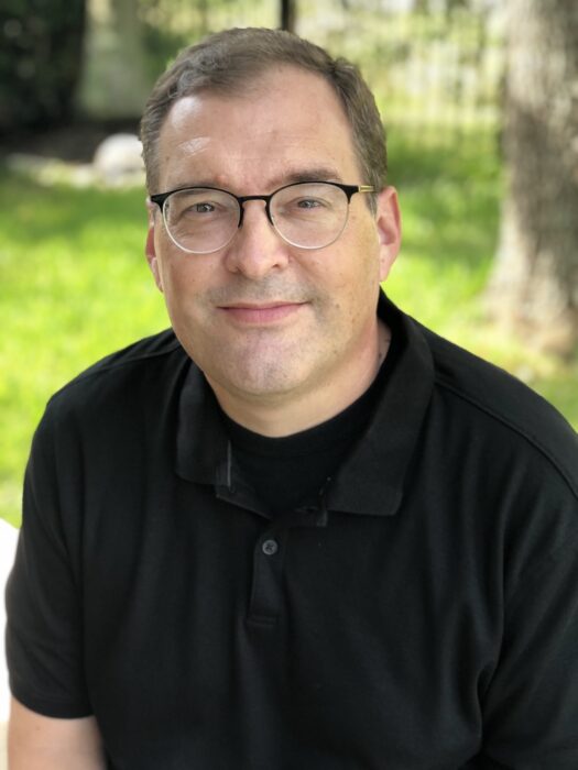Man wearing glasses and black shirt sits outdoors